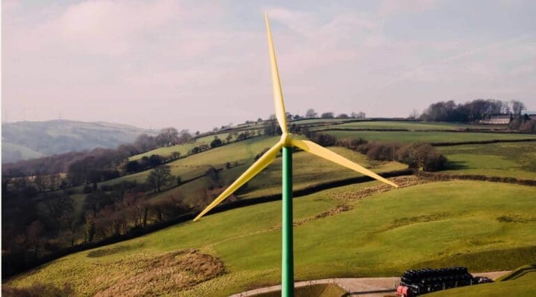 A windmill towers against a backdrop of rolling green fields